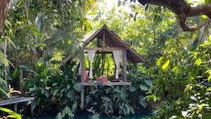 A wooden gazebo structure with a roof and white curtains, surrounded by lush greenery and a clear pool. - Tung Homestay (Nan)