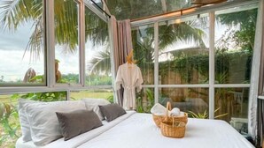 A bedroom with a bed, pillows, a basket, and a window with curtains. - Tung Homestay (Nan)
