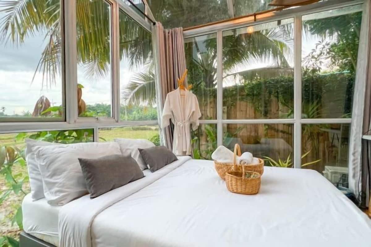 A bedroom with a bed, pillows, a basket, and a window with curtains.