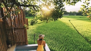 A person in a yellow swimsuit sitting by a pool with bamboo walls and a view of a green field. - Tung Homestay (Nan)
