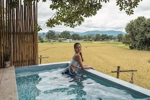 A person in a hot tub with a view of a rice field and mountains. - Tung Homestay (Nan)