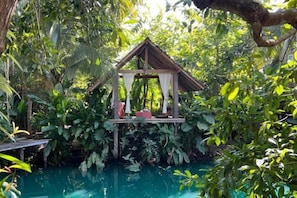 A gazebo structure with a roof and a platform, surrounded by lush greenery and a pool. - Tung Homestay (Nan)