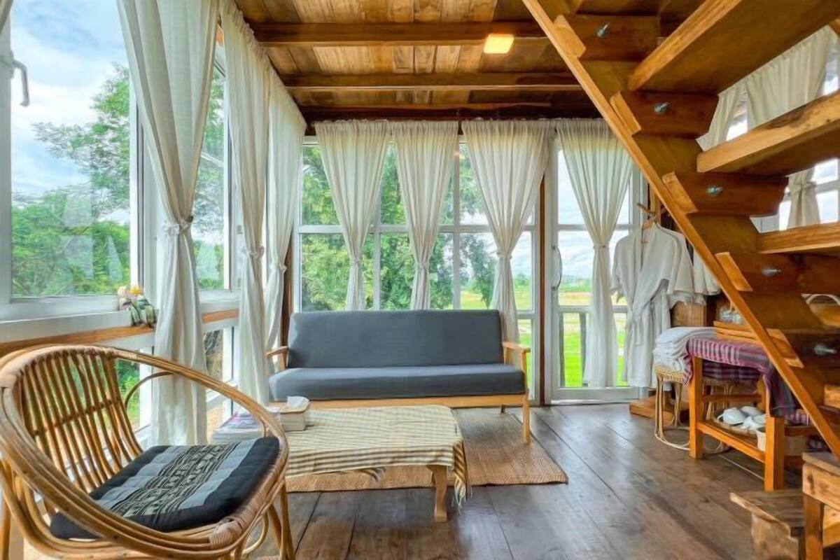 A room with a wooden ceiling, a sofa, a wicker chair, a small table, and a wooden shelf with items.