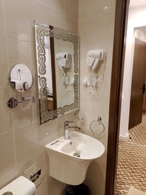 Un baño con lavamanos, espejo, secador de pelo y tozaleta.