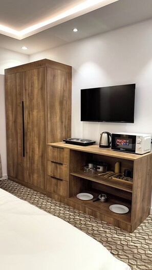 Habitación de hotel con armario de madera, televisor de pantalla plana, kitchenette con microondas y cama con alfombra estampada.