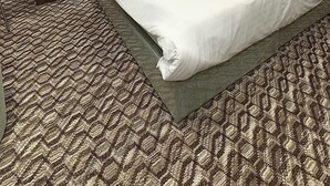 Une chambre d’hôtel avec un grand lit, deux tables de chevet, une tête de lit, un tableau au mur, une chaise et une moquette à motifs.
