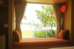 Una habitación con un asiento junto a la ventana, cortinas y vistas a zonas verdes.