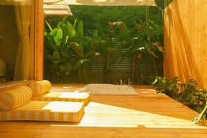 Una terraza de madera con sofá y bañera, rodeada de abundante vegetación.