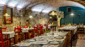 Ein Restaurant mit Steinsälen, Holztischen und roten Stühlen.