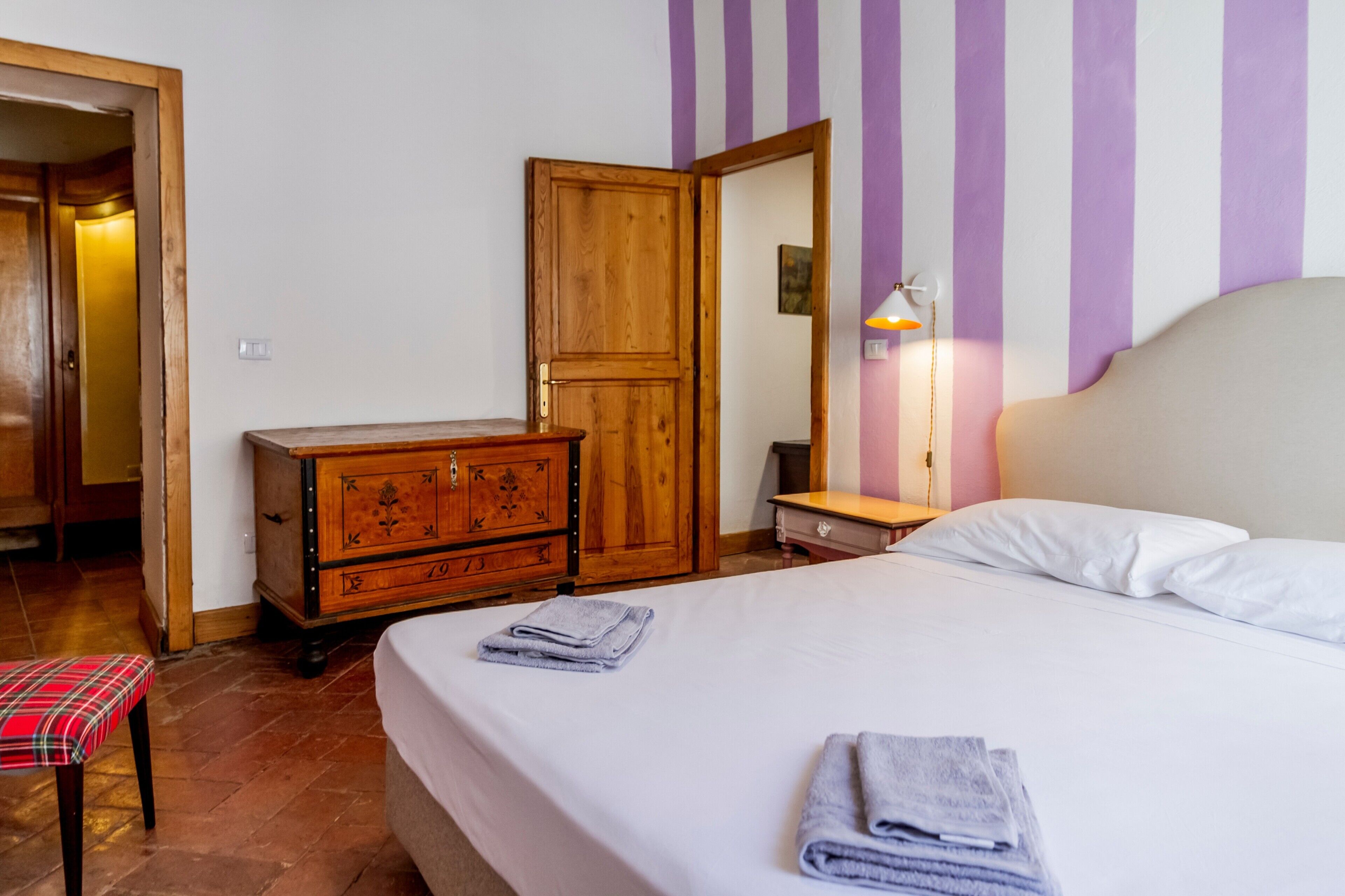 Une chambre à coucher comprenant un lit, une commode en bois, un banc et une porte donnant sur une autre pièce.