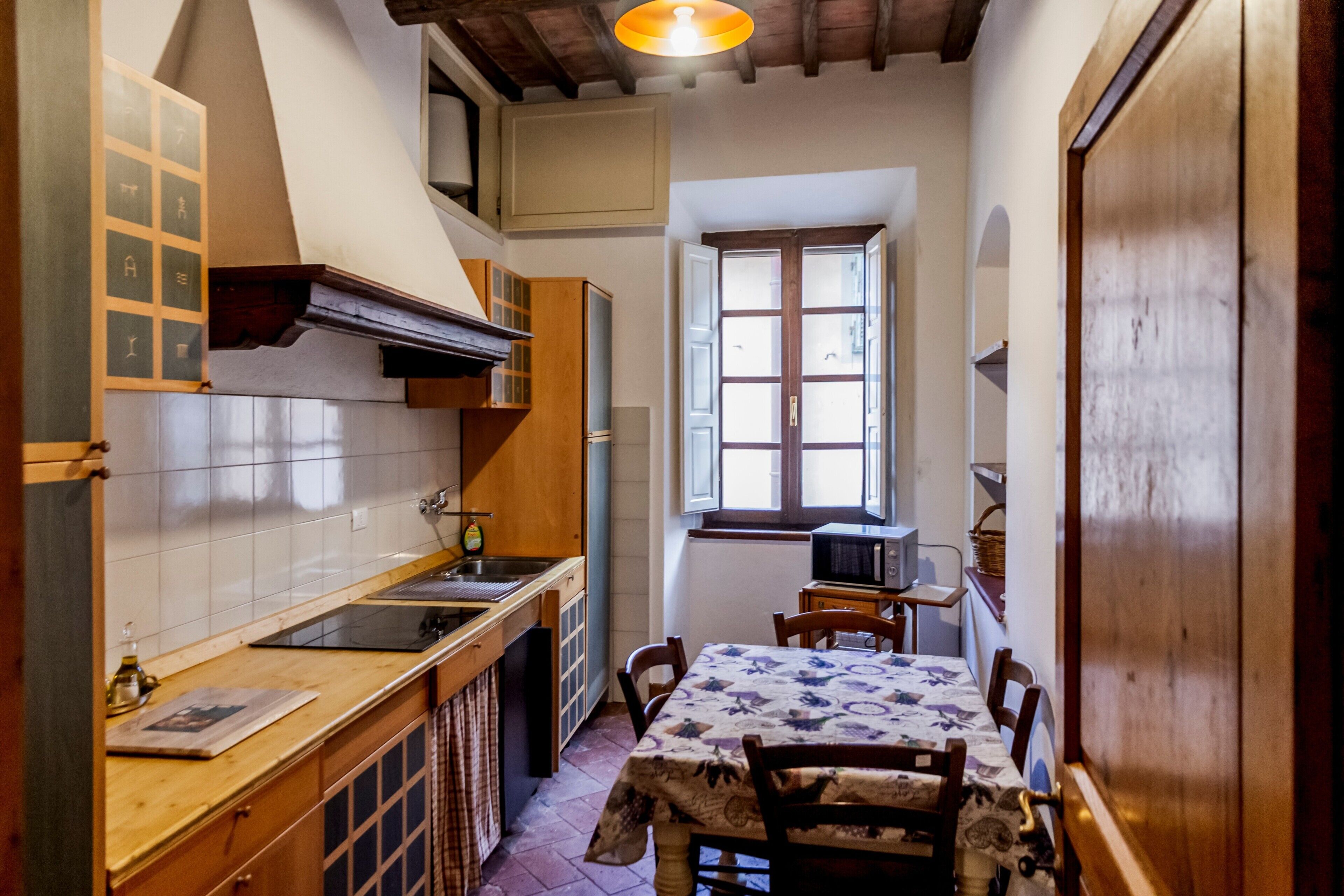 A narrow kitchen with a wooden countertop, a stove, and a dining table with chairs.