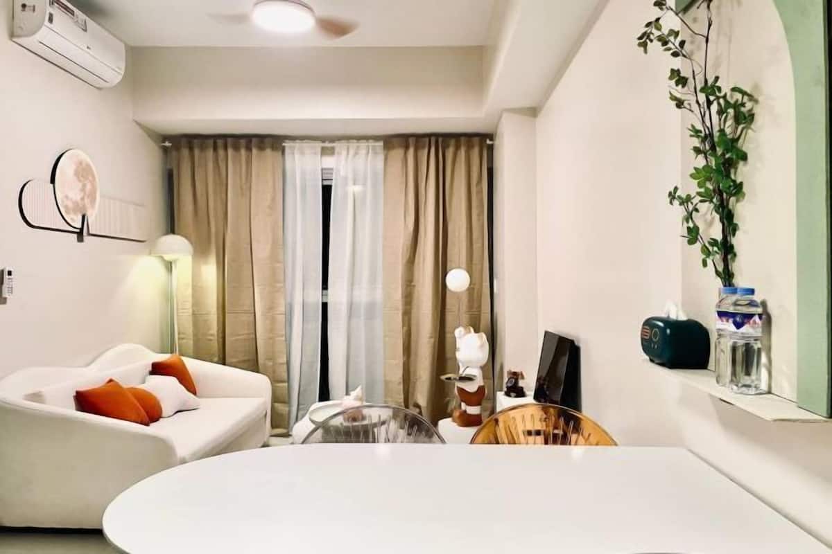 Un salon moderne avec un canapé blanc, une table basse ronde, une petite table à manger et une plante décorative.