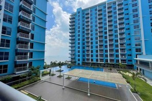 Un edificio de gran altura con varios balcones, una zona de piscina en la azotea y cielo despejado.