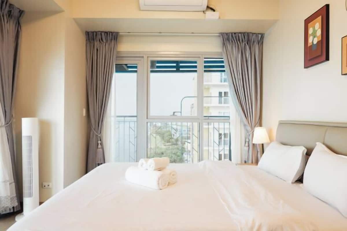 Une chambre d’hôtel avec un grand lit, une table de chevet avec une lampe et une fenêtre avec des rideaux.