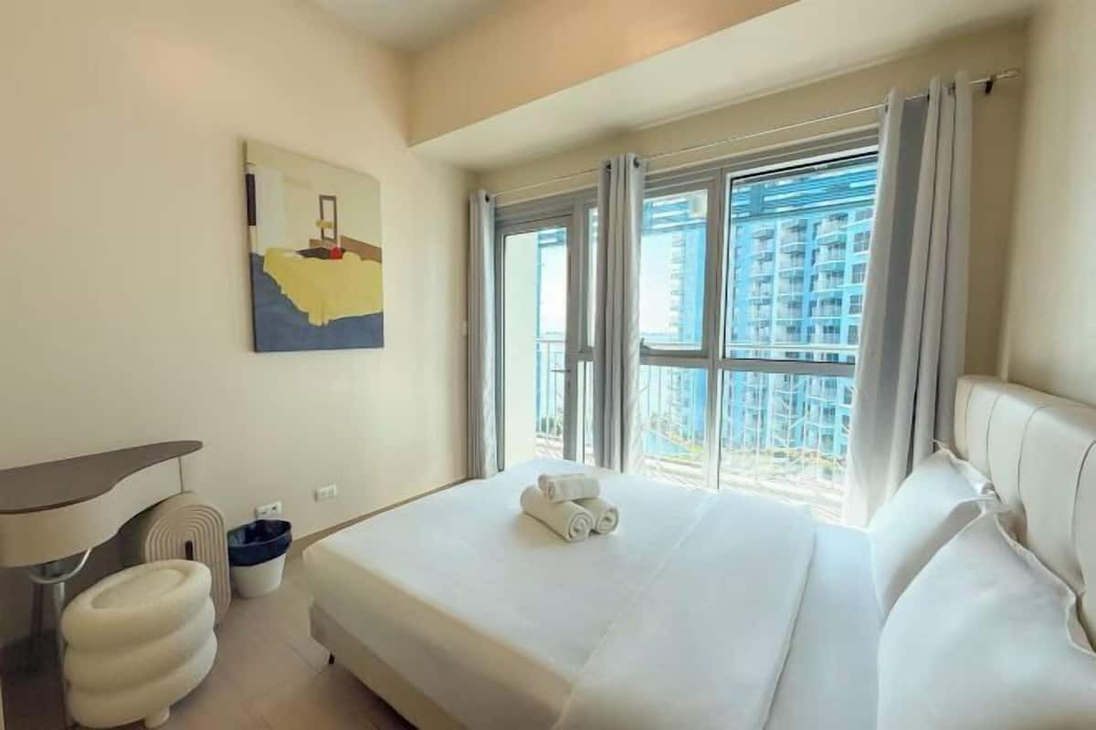 Une chambre d’hôtel avec un lit, un bureau, une chaise et une fenêtre donnant sur des immeubles.