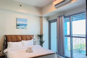 A hotel room with a bed, a painting, a potted plant, and a sliding glass door to the outside. - Thompson Suites Okada (Bayshore 2 Residence) (Paranaque)