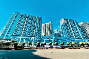 A high-rise building with multiple floors, a clear sky, and a well-maintained landscaped area with trees. - Thompson Suites Okada (Bayshore 2 Residence) (Paranaque)