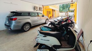 A parking garage with a silver minivan and several scooters. - Dhanas Residency Auroville (Kuilapalayam)