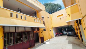 A yellow building with a gated entrance, a covered parking area, and a visible car. - Dhanas Residency Auroville (Kuilapalayam)