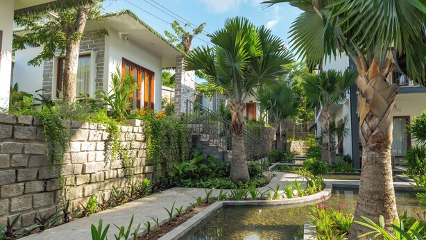 A residential property with a stone wall, a small garden with various plants, a paved pathway, and a central water feature. - Pandora Sand Hill Mui Ne Resort (Mui Ne)