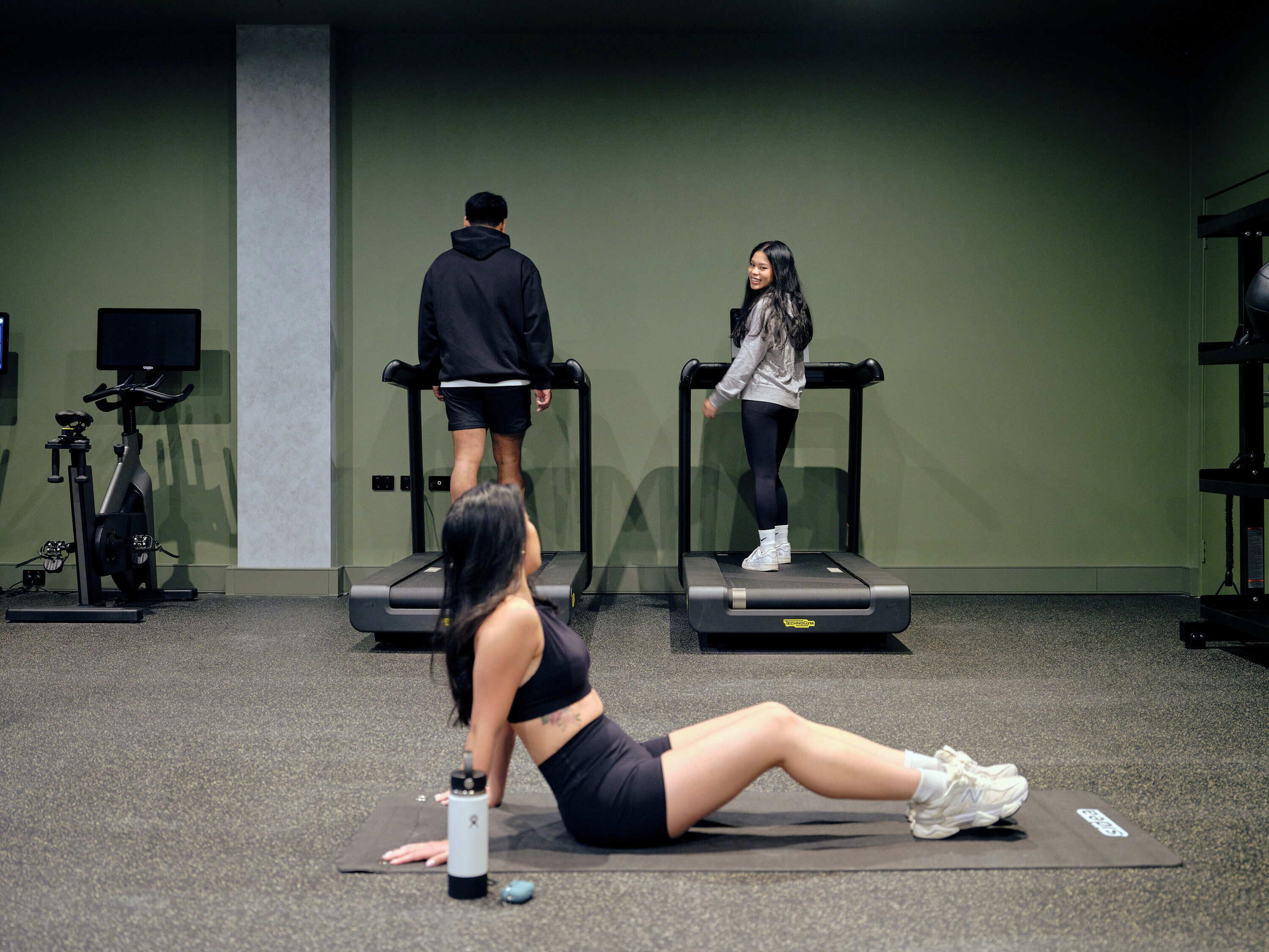 Une salle de sport équipée de tapis de course, d’un vélo d’appartement et d’un tapis de yoga posé sur le sol.