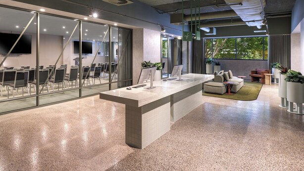 Un espacio de oficina moderno con una larga barra, paredes de vidrio y una zona de estar con sofá y sillones.