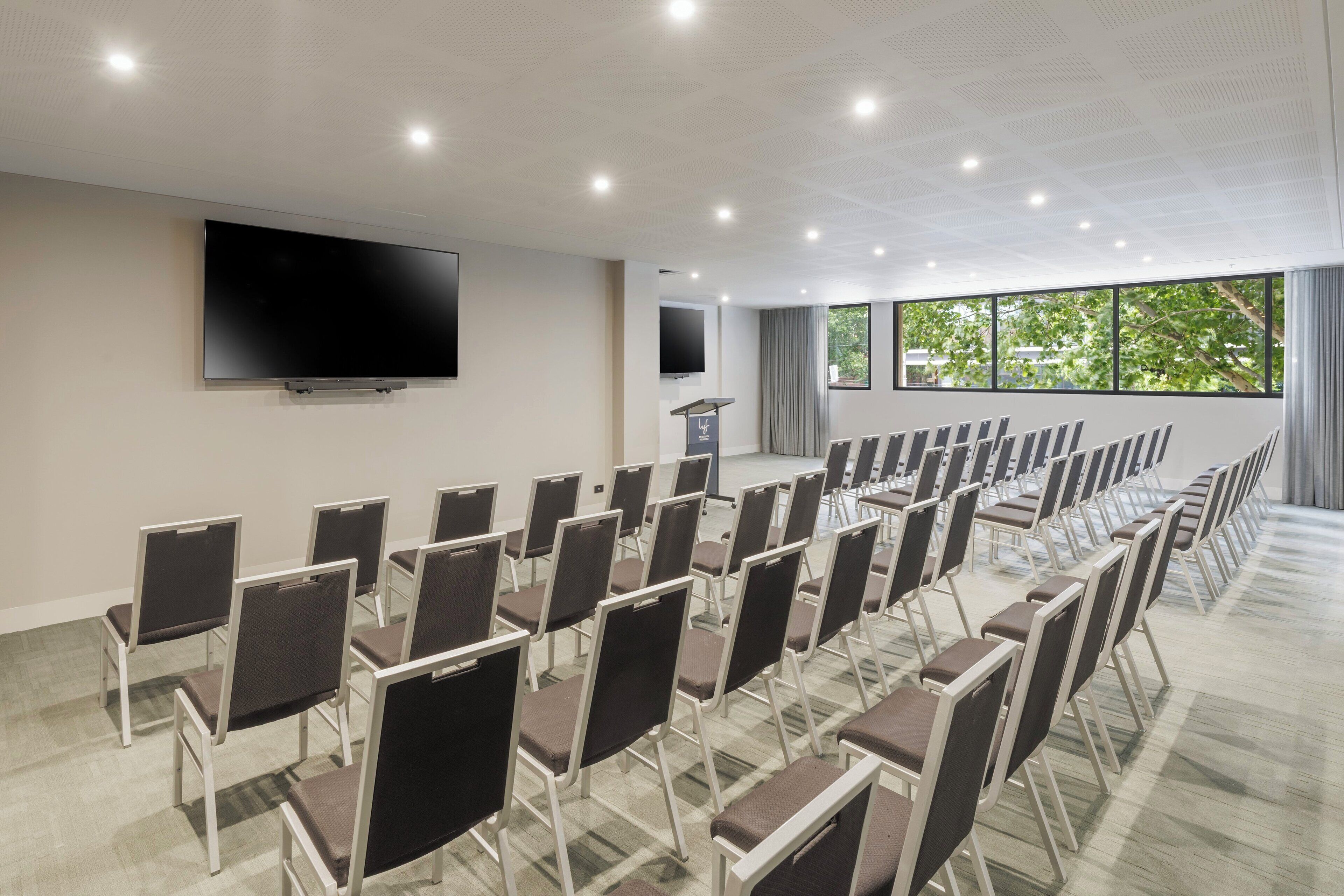 A conference room with rows of chairs, a large flat-screen TV, and a podium.