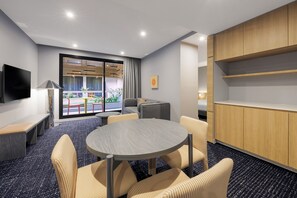 Une chambre d’hôtel moderne avec une table ronde, des fauteuils confortables, un téléviseur à écran plat, un canapé et une grande fenêtre donnant sur l’extérieur.