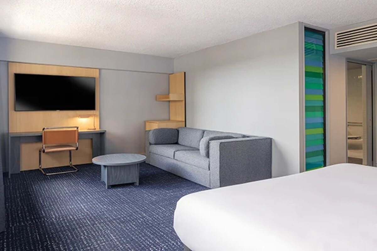 A hotel room with a bed, a sofa, a small round table, a TV, and a wardrobe.