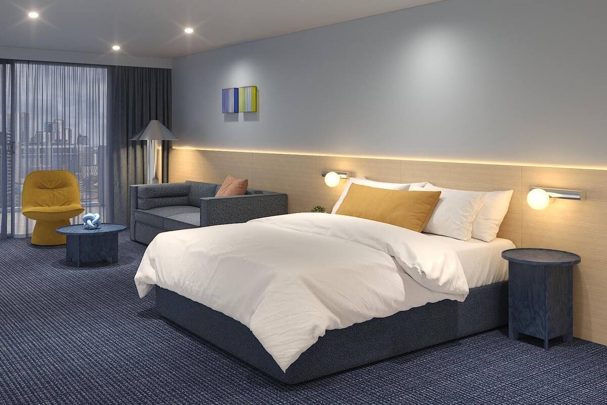 A modern hotel room with a large bed, a sofa, a chair, and a view of the city skyline through the window.