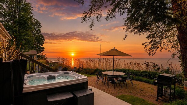 A hot tub, outdoor seating, and a view of the sunset over the ocean. - Lake Erie Beachfront Retreat - 8 BR + Private Beach & Hot tub! (Madison)