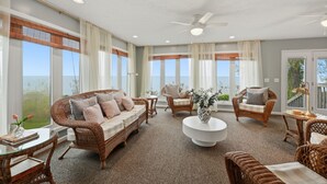 A spacious living area with wicker furniture, large windows, and a ceiling fan. - Lake Erie Beachfront Retreat - 8 BR + Private Beach & Hot tub! (Madison)