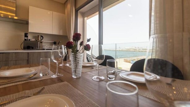 A dining table set for two with a view of the sea through large windows. - Horizon Marina terrace (Casablanca)