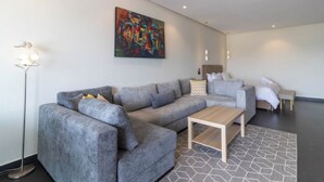 A modern living room with a grey sectional sofa, a wooden coffee table, and a colorful abstract painting on the wall. - Horizon Marina terrace (Casablanca)