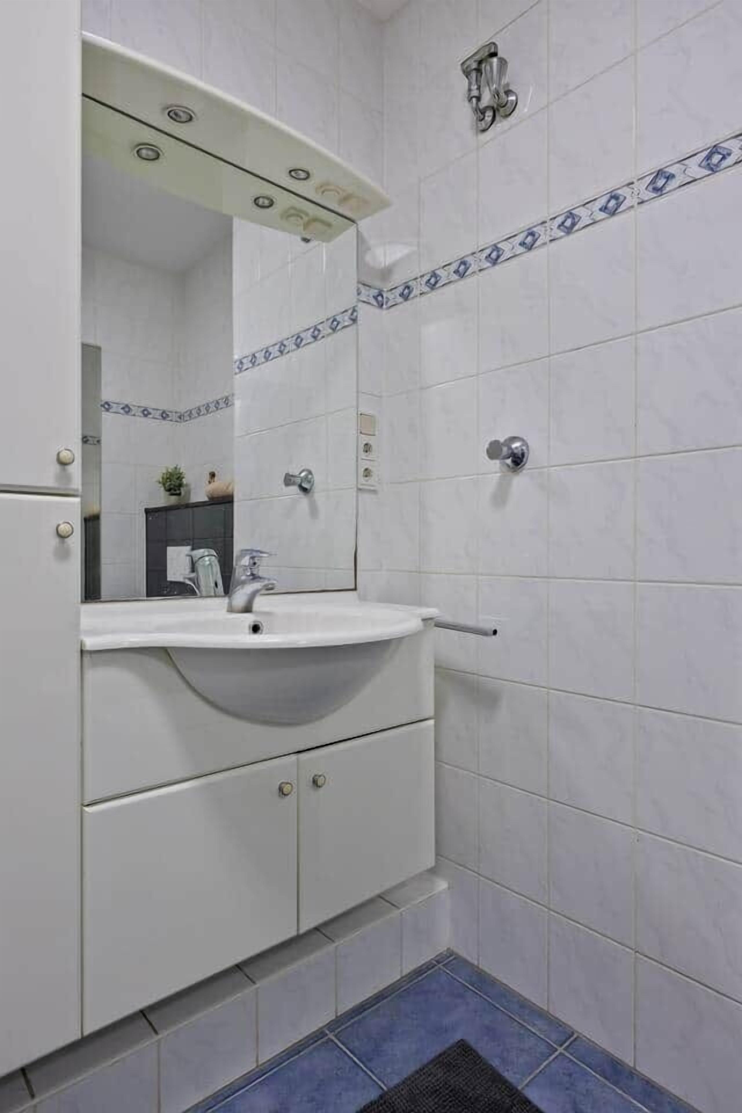 Un baño con azulejos blancos, un lavabo con espejo y una zona de ducha.