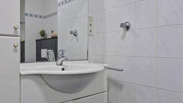 Un baño con azulejos blancos, un lavabo con espejo y una zona de ducha.