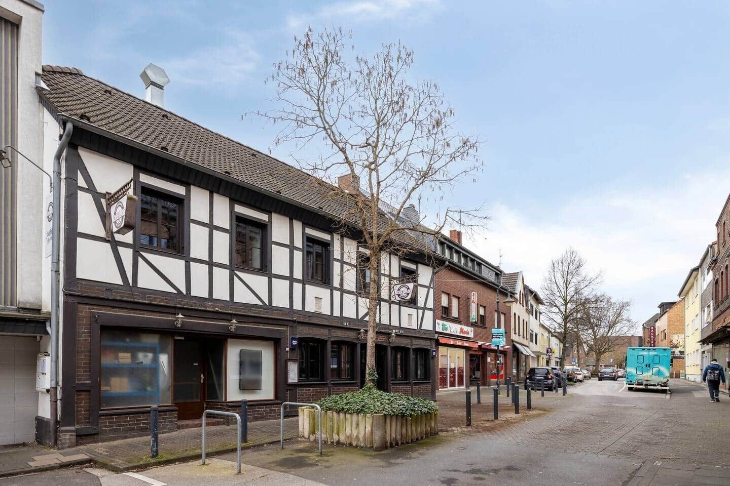 Une rue bordée de bâtiments traditionnels à colombages, un fourgon garé et un ciel dégagé.