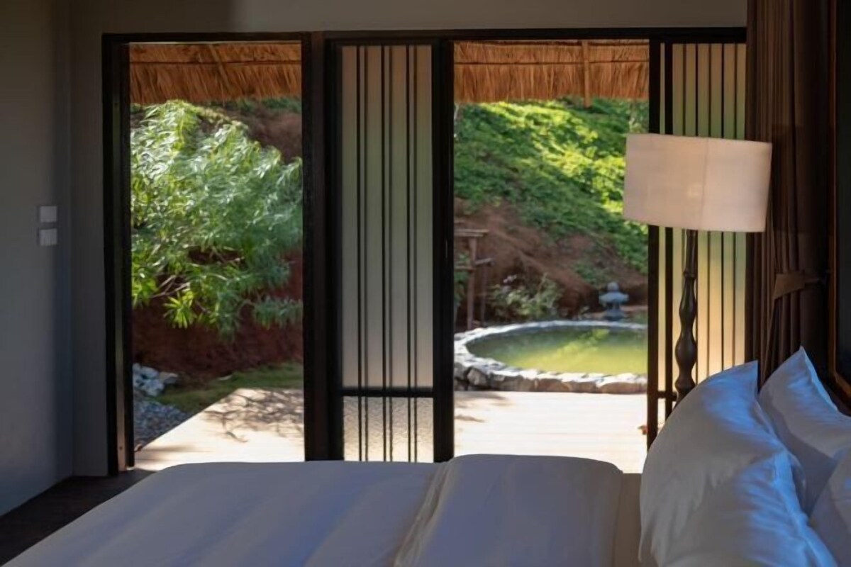 Una stanza con un letto, una lampada e vista su un giardino con uno stagno.
