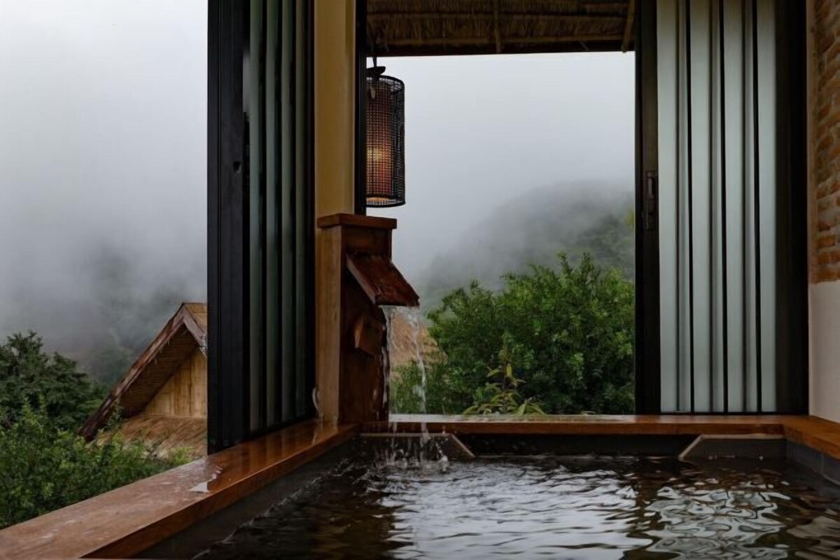 A traditional Japanese-style room with a wooden water feature, sliding doors, and a view of a forested area.