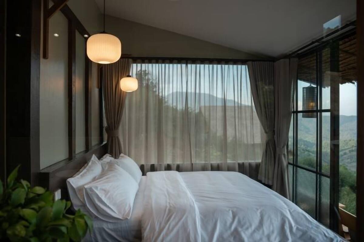 A bedroom with a large bed, sheer curtains, and a view of the outdoors.