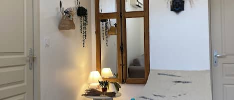 Una habitación con un espejo de marco de madera, una mesita con lámparas, una figura decorativa y un tapete de bienvenida.
