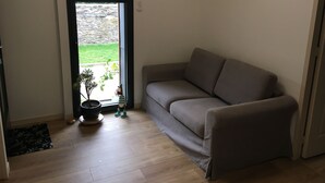 Una habitación con un sofá gris, una planta en maceta y vistas a un muro de piedra y césped.