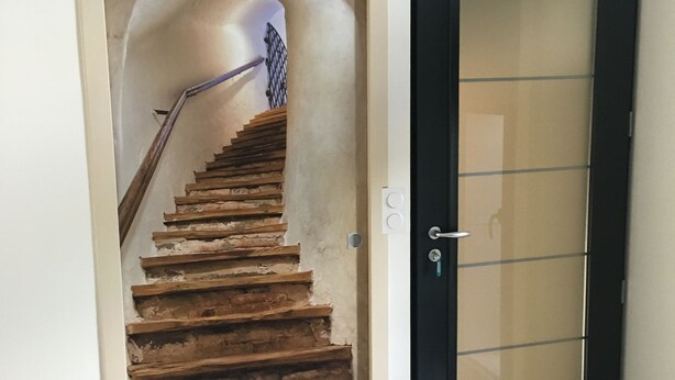 Una escalera con escalones de madera que conduce a un piso superior, una puerta negra con un panel de vidrio y una pequeña alfombra en el suelo.