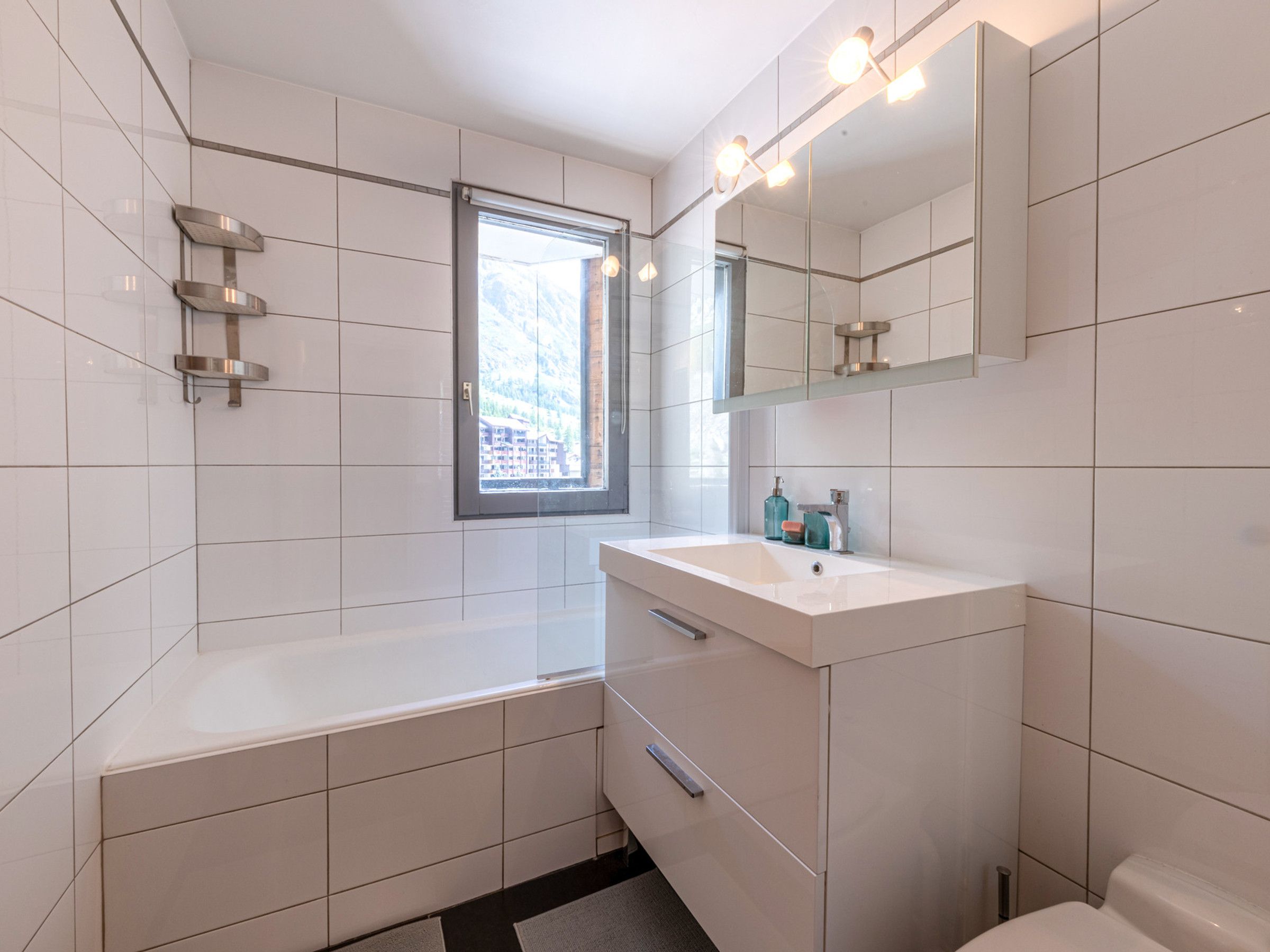 A modern bathroom with a bathtub, a vanity with a mirror, and a window providing a view of buildings outside.