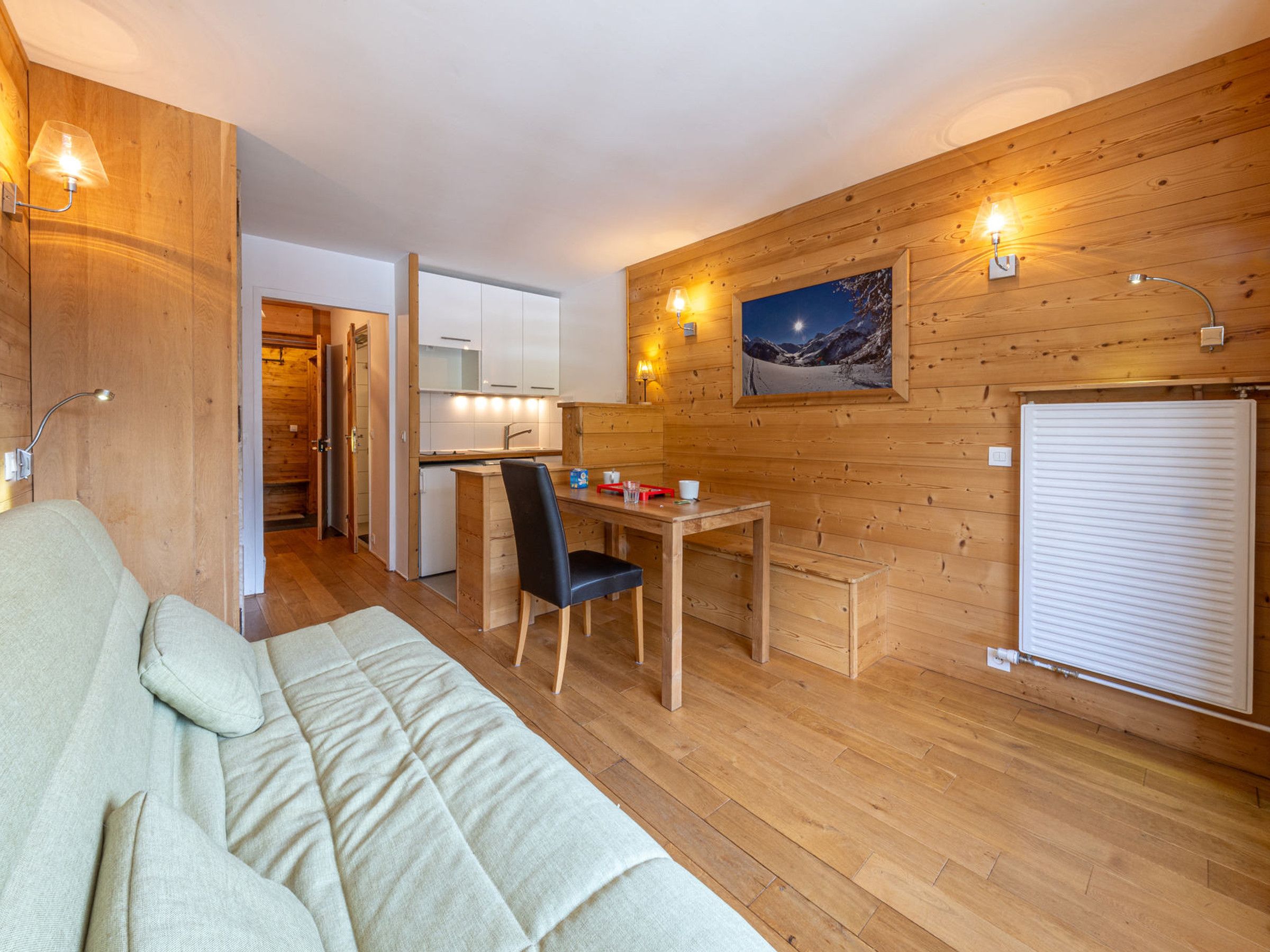 A cozy room with a sofa, a wooden dining table with chairs, a small kitchen area, and a radiator.