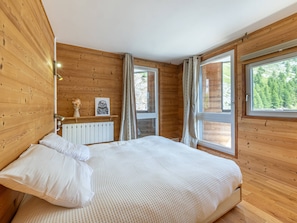 A wooden cabin bedroom with a bed, a radiator, a window, and a view of trees.