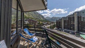 En balkong med två blå solstolar, utsikt över ett bergskedja och en modern byggnad i bakgrunden.