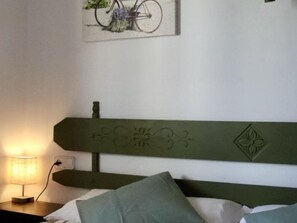 Quarto com cabeceira verde, luminária de cabeceira e quadro na parede.