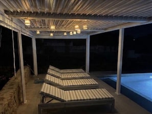 Uma área externa coberta com espreguiçadeiras e piscina.