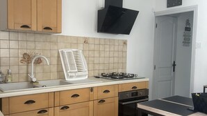 A compact kitchen with wooden cabinets, a gas stove, a sink, and a black range hood. - T2 in charming Ardèchois village (SAINT-JULIEN-EN-SAINT-ALBAN)